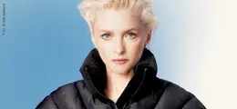 Alison Goldfrapp mit entschlossenem Blick, trägt eine schwarze Jacke. Hintergrund ist blau-weiß verschwommen.