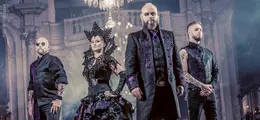 Vier Personen posieren in stilvollen, dunklen Outfits in einem eleganten, beleuchteten Raum.