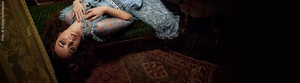 „Laufey A Matter Of Time“ in eleganter Schrift. Frau liegt in blauer Spitze auf vintage Sofa, neben einem Tisch.