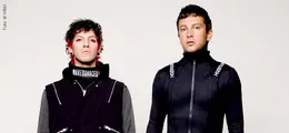 Zwei Personen in dunkler Kleidung mit Aufschrift „MONCLER“ auf ihren Oberteilen.