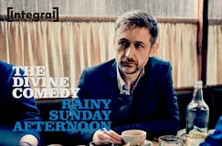 Text: The Divine Comedy, Rainy Sunday Afternoon. Ein Mann sitzt an einem Tisch mit einer Tasse und Flaschen.