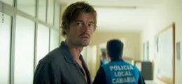 Ein Mann in einem Flur schaut besorgt zurück. Eine Person mit "POLICIA LOCAL CANARIA" auf der Jacke geht voraus.