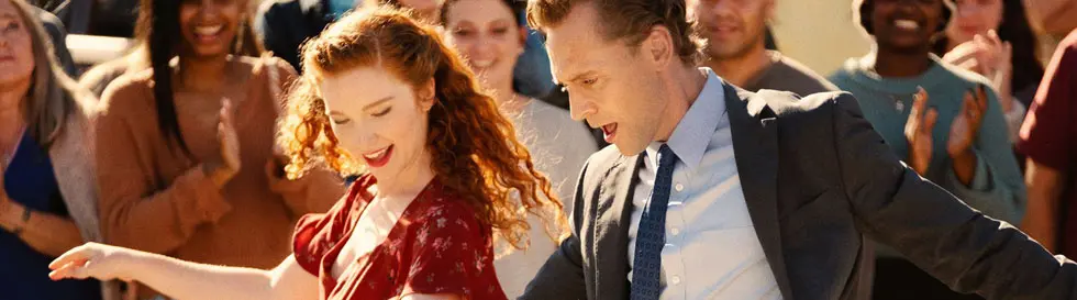 Zwei Personen tanzen inmitten einer fröhlichen Menschenmenge im Freien.