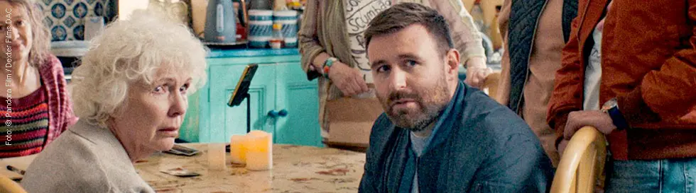 Eine Gruppe älterer Menschen sitzt um einen Küchentisch. Die Atmosphäre wirkt gemütlich und vertraut.