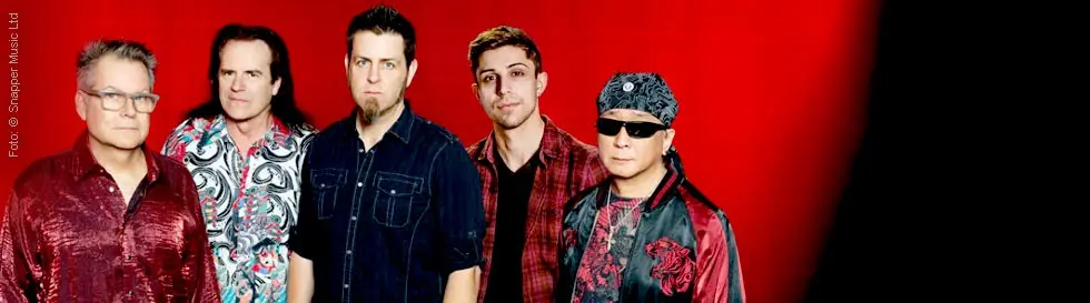 Fünf Männer in auffälliger Kleidung vor einem leuchtend roten Hintergrund.