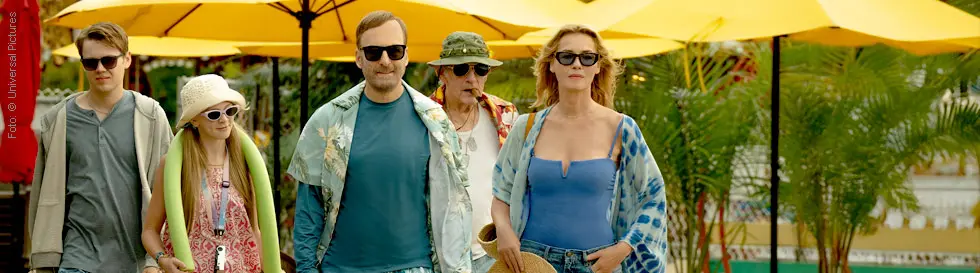 Fünf Personen in Sommerkleidung und Sonnenbrillen vor gelben Sonnenschirmen.