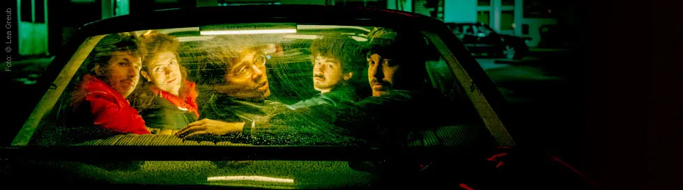 Fünf Personen sitzen beengt auf einem Rücksitz, durch die Heckscheibe sichtbar.