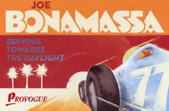 "JOE BONAMASSA", "DRIVING TOWARDS THE DAYLIGHT", "PROVOGUE". Illustration von Rennauto und Palmen im Sonnenuntergang.