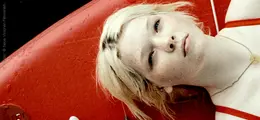 Eine junge Frau mit blonden Haaren liegt auf einem roten Boot. Sie trägt ein rotes Oberteil.