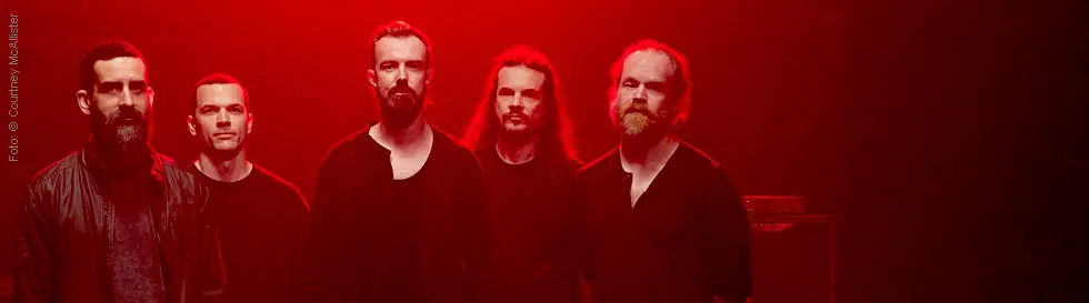 Fünf Männer in schwarzer Kleidung stehen in rot beleuchtetem Raum.