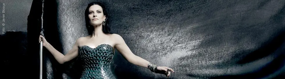 Eine Frau in einem dunklen, schimmernden Kleid steht mit einem langen Stab vor einem düsteren Hintergrund.