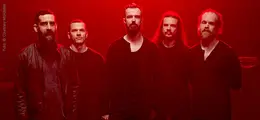 Fünf Männer in schwarzer Kleidung stehen in rot beleuchtetem Raum.