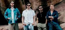 Vier Männer stehen vor einem Felsen. Sie tragen lässige Kleidung und Sonnenbrillen.