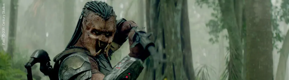 Ein außerirdisches Wesen mit Dreadlocks und Rüstung steht kampfbereit im dichten Dschungel.