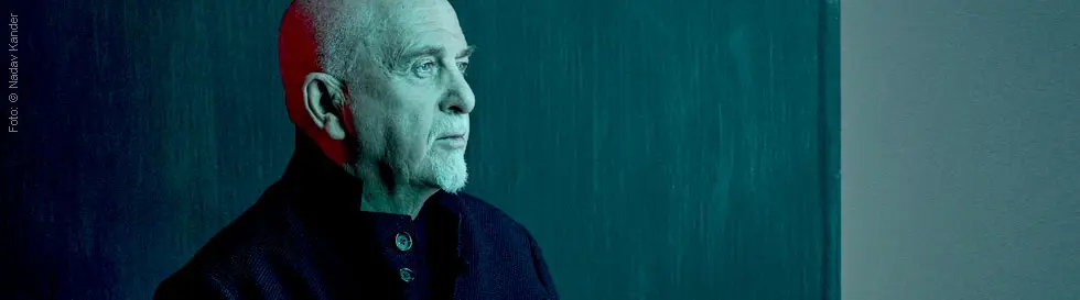 Ein Mann mit Glatze und grauem Kinnbart blickt zur Seite, in blau-rotem Licht.