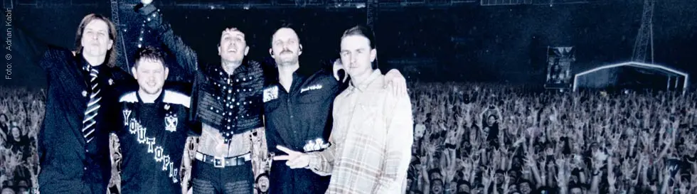 Fünf Personen stehen auf einer Bühne vor einer jubelnden Menschenmenge.