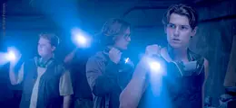 Drei junge Menschen mit Taschenlampen in einem dunklen Raum, angespannt und aufmerksam.
