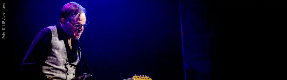 Ein Musiker spielt E-Gitarre in blauem Bühnenlicht.
