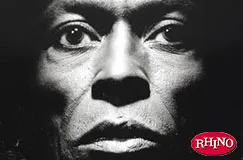 Nahaufnahme eines Gesichts in Schwarz-Weiß, mit intensiven Augen. Das Logo "RHINO" ist unten rechts. 