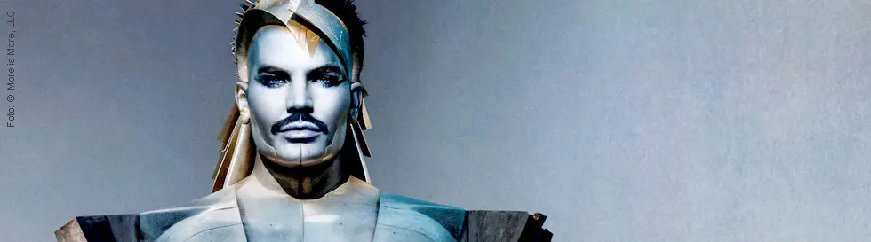 Ein an­d­ro­gyn wirkender Mensch in metallisch-futuristischer Rüstung, mit kantigen Formen und stacheliger Kopfverzierung.