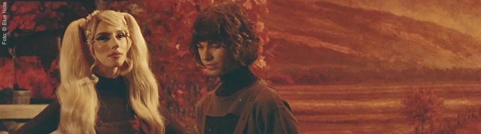 Foto von zwei Menschen im Vintage-Stil, umgeben von herbstlichen Farben; eine Person hat lange, blonde Haare.