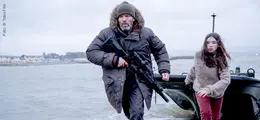 Ein Mann mit Gewehr und ein Mädchen eilen aus einem Boot ans Ufer.