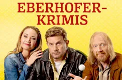 "Eberhofer-Krimis" in roter Schrift auf gelbem Hintergrund. Drei Personen lächelnd, mittig ein Mann in Polizeilederjacke.