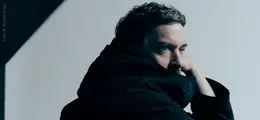 Ein Mensch in dunkler Kleidung blickt nachdenklich zur Seite in Richtung Lichtquelle. Links ist ein diagonaler Schatten.