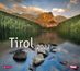 "Tirol 2027". Ein klarer Bergsee mit Felsen im Vordergrund, umliegende Wälder und ein großer, von der Sonne beleuchteter Berg.