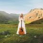 Eine Frau in weißem Kleid steht auf einer Wiese mit Gitarre in der Hand vor einer bergigen Landschaft im Hintergrund., LP