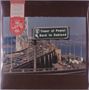 Ein Straßenschild zeigt „Tower of Power Back to Oakland“. Darunter eine befahrene Brücke über Wasser in einer urbanen Umgebung., LP