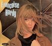 Françoise Hardy. Eine Frau mit langem Haar hält einen Regenschirm, trägt einen Mantel, schaut nachdenklich.
