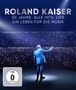 ROLAND KAISER. 50 JAHRE. ALLE HITS. LIVE. Ein Mann im blauen Anzug steht vor einem großen Publikum mit Lichtern.