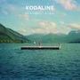 Cover von Kodaline "In a Perfect World". Ein Holzsteg mit Personen darauf schwimmt auf einem großen See, umgeben von Bergen.