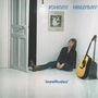 Text: „JOHNNY HALLYDAY insolitudes“. Ein Mann sitzt in einem weißen Raum, eine Gitarre steht daneben.