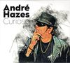 "Curiosa. André Hazes. Illustration eines Mannes mit Hut, Sonnenbrille und Goldkette, in nachdenklicher Pose."