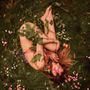 Eine Person liegt nackt in einem Bett aus Gras und Blumen, mit Pflanzen bedeckt., CD