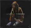 Text: "carla bruni à l'Olympia". Frau mit Gitarre, sitzt lächelnd, lange Haare, dunkler Hintergrund.