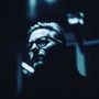 Ein Mann mit Brille in blauem Licht, ernstes Gesicht, starker Schatten, kunstvolle Beleuchtung, im Dunkeln.