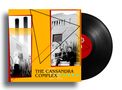 Auf gelbem Hintergrund steht "THE CASSANDRA COMPLEX". Schwarz-weiße Fotos von Personen und Gebäuden. Eine Schallplatte., LP