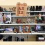 Text: "GIRLTROUBLE AS IS".   
Regal mit Schuhen, Dekorationen und Haushaltswaren., LP