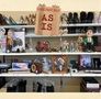 Der Text "AS IS" steht auf einem Schild. Darunter Schuhe, Figuren und diverse Gegenstände auf Regalen., CD