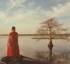 Kein Text zu sehen. Frau in rotem Kleid auf Bootsbug steht im Wasser neben einem kahlen Baum, unter blauem Himmel., CD