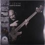 "TONY LEVIN: DOWN TO THE BASS" in weißen Buchstaben. Mann spielt Bass, ernster Gesichtsausdruck, Retro-Stil.