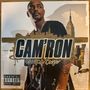 Text: "CAM'RON Crime Pays". Darstellung eines Mannes vor einer Skyline, mit hohem Gebäude im Hintergrund.