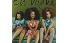 Text "En Vogue". Drei Frauen sitzen modisch gekleidet auf einem Sofa, mit auffälligen Frisuren und Kleidung in Blumenmustern.