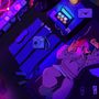 Eine Person liegt in Neonlicht auf einem Bett, hält ein Smartphone, umgeben von Kamera, Socken und Brief mit Herz., CD