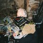 "DELTA5, AFCC, BFCC" stehen auf Papier. Ein Mensch hält Synthesizer voller bunter Kabel in einem steinigen Raum., LP