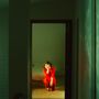 Es gibt keinen Text. Eine Frau in einem roten Kleid kauert nachdenklich in einem beleuchteten Türrahmen., CD