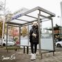 Ein Wartehäuschen mit dem Schild "TRAIN DE VIE". Eine Person in Winterkleidung steht darin auf einem Bürgersteig., CD